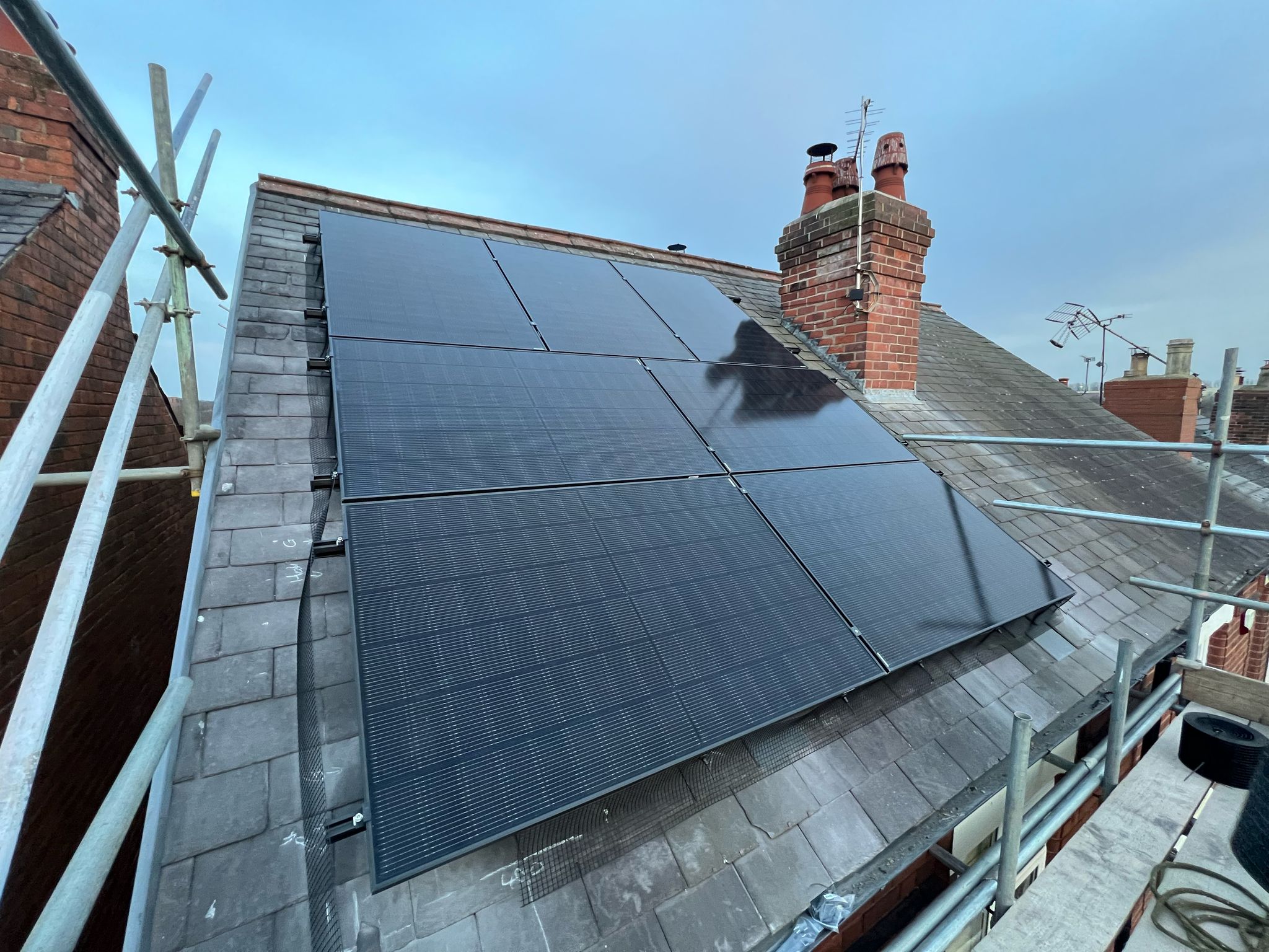 Solar panels on a slate roof beside a chimney stack, with scaffolding along the edge