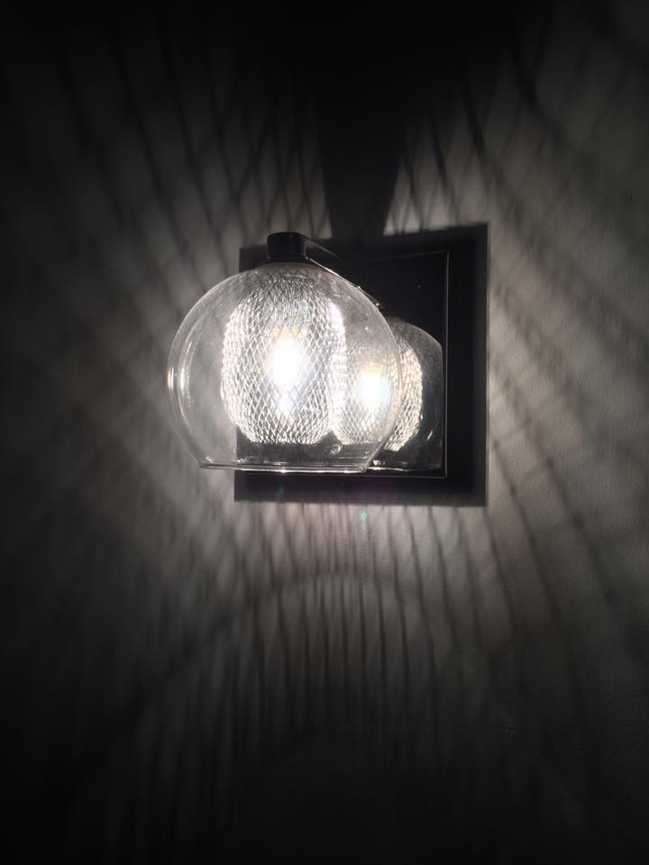 A glass globe wall light switched on, casting a patterned glow across a dark wall