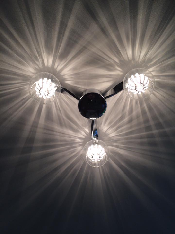 A three-arm ceiling light with glass globes switched on, throwing star-shaped light across the ceiling