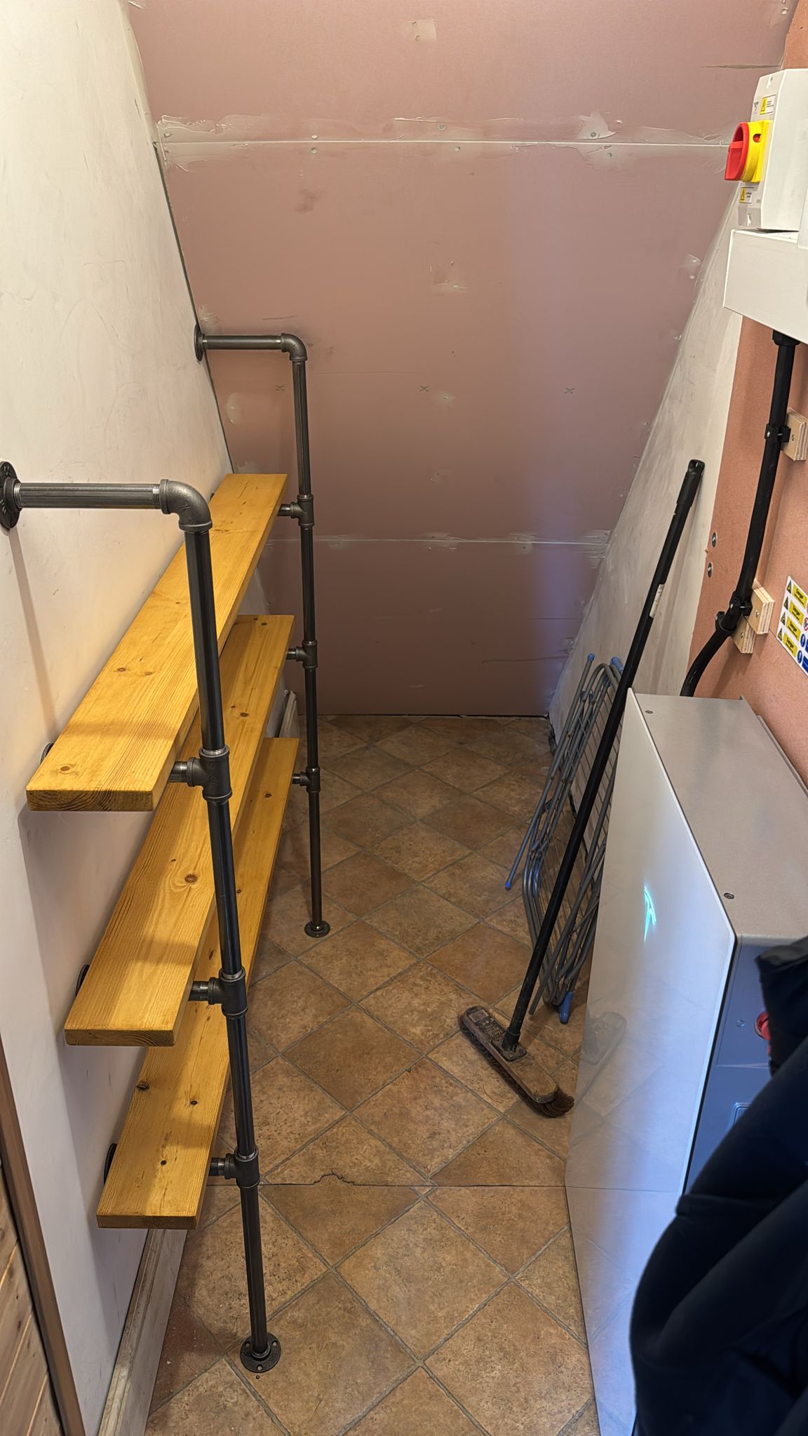 A home battery installed in a tidy under-stairs space beside timber and pipe shelving